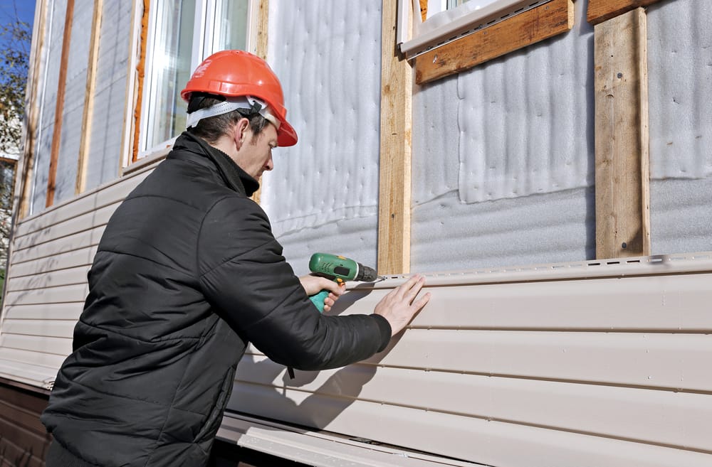 A siding specialist uses a power drill to fasten vinyl siding panels to the exterior studs of a home during renovation. The installation process ensures proper insulation, structural support, and long-term durability – Siding Installation in Indianapolis.
