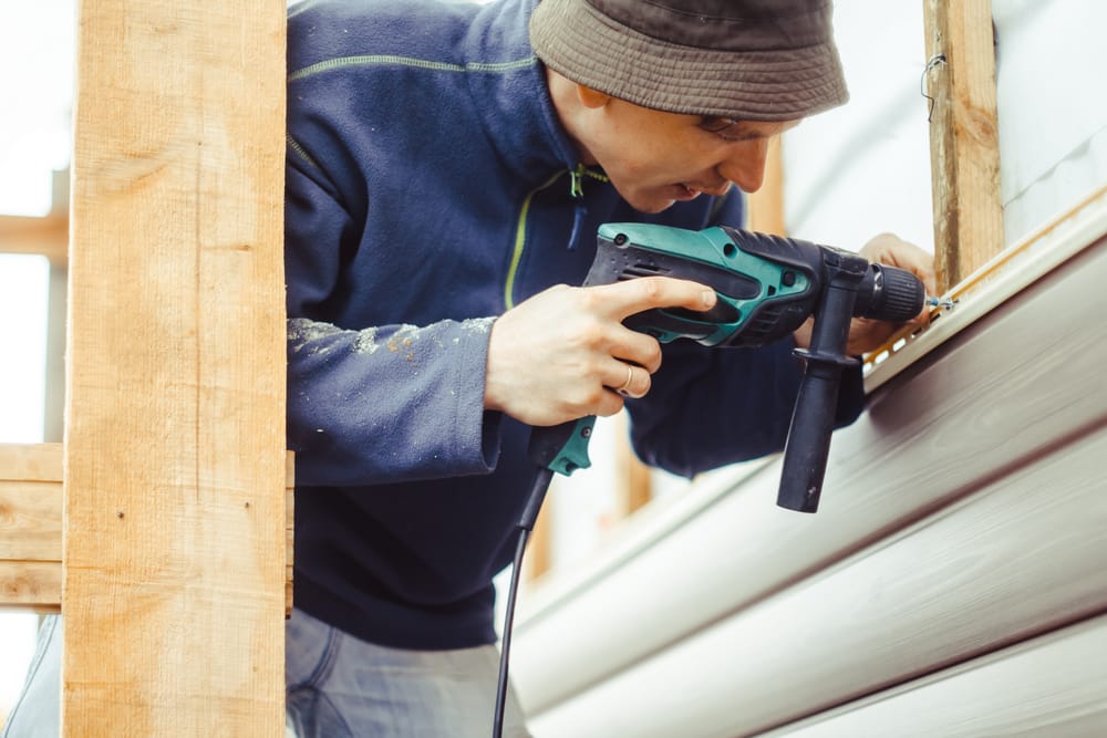 A worker uses a power drill to secure loose siding panels to the exterior frame, ensuring stability and proper alignment as part of a detailed siding repair process – Siding Repair in Indianapolis.