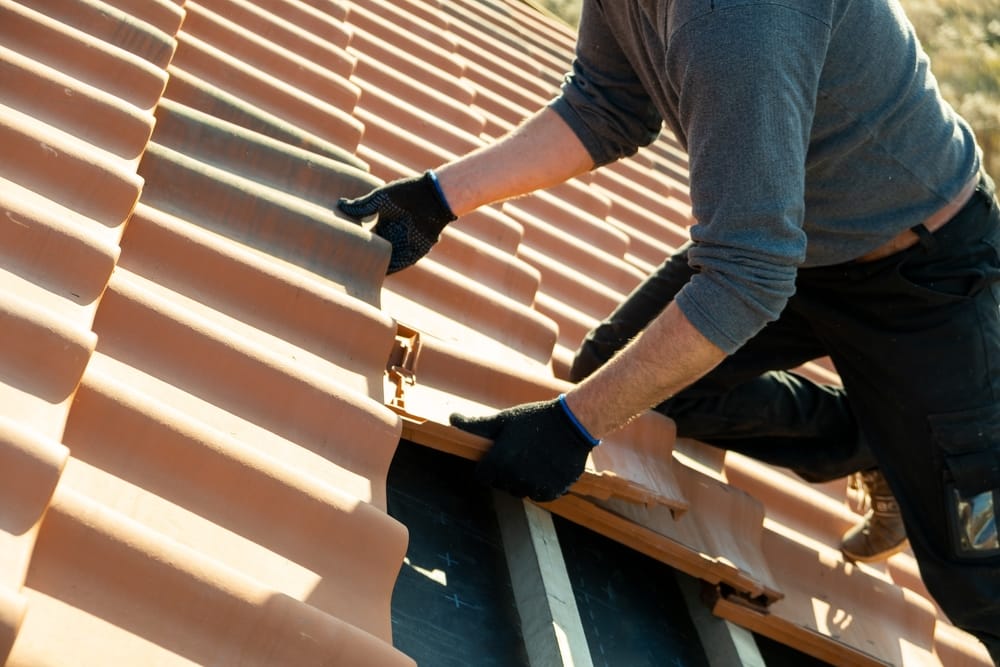 A roofer installs new clay roof panels, securing each piece onto the roof structure during a replacement job. The image highlights careful craftsmanship and detailed installation work. – Roof Replacement in Indianapolis
