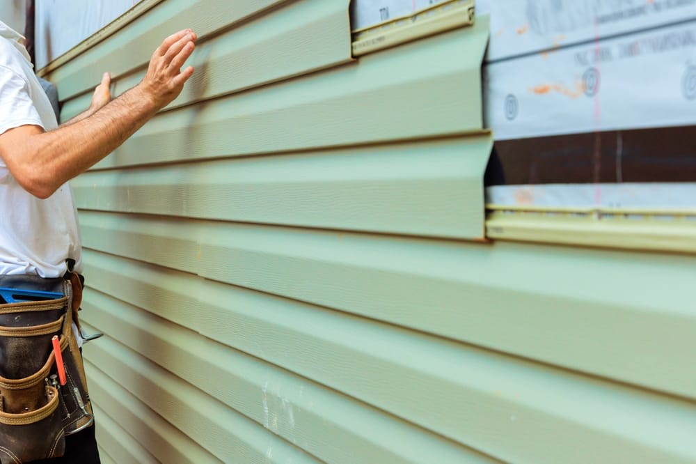 A contractor carefully aligns and installs new vinyl siding panels on a home exterior, ensuring a secure and uniform fit. The worker uses precision and proper tools to achieve a clean, weather-resistant siding finish – Siding Installation in Indianapolis.