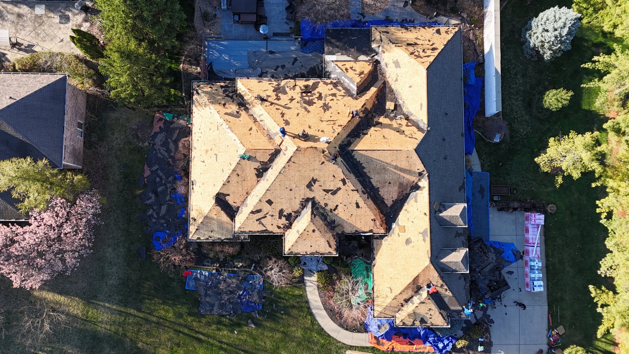 Aerial view of a house with roof repair in progress, showing workers removing shingles and protective tarps covering the surrounding area - Copes R&R Construction Aerial view of a house with roof repair in progress, showing workers removing shingles and protective tarps covering the surrounding area - Copes R&R Construction
