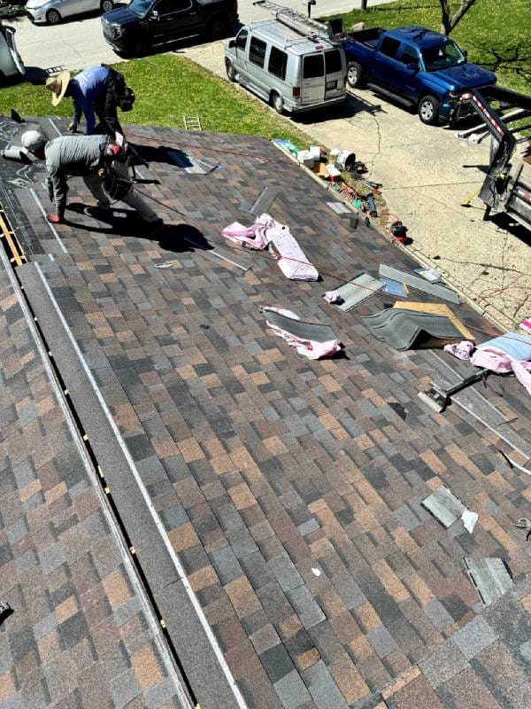 Workers installing shingles on a roof during a roofing project, with tools and materials scattered nearby - Copes R&R Construction Workers installing shingles on a roof during a roofing project, with tools and materials scattered nearby - Copes R&R Construction
