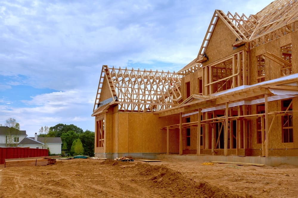 A partially framed multi-story home under construction, featuring structural wood beams, roof trusses, and open framing. The large worksite showcases the beginning phases of building a new residential property – General Housing Construction.