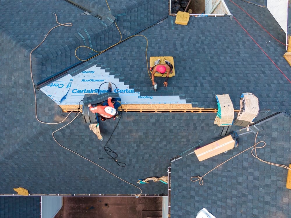 A top-down look at a commercial roofing team installing new shingles and underlayment on a large building. Tools, materials, and safety lines show an active professional roofing project – Commercial Roofing in Indianapolis.