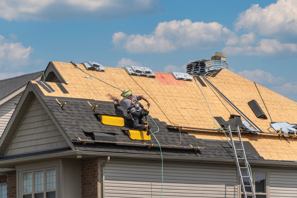 A roofer installs new shingles on a partially stripped roof deck, using safety ropes and tools to complete the repair. The image captures the detailed process of restoring roof integrity – Roof Repair in Indianapolis.