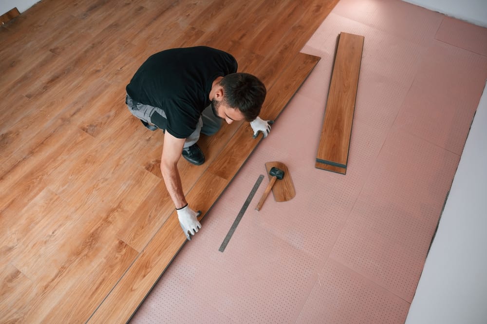 A professional carefully fits vinyl plank pieces together over a pink underlayment layer, showcasing the step-by-step process of installing durable, water-resistant flooring in a residential space – Flooring.