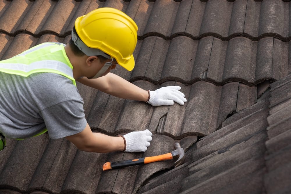 A roofing technician wearing safety gear carefully adjusts damaged roof tiles on a commercial roof. The close-up view highlights professional repair work designed to maintain structural integrity – Commercial Roofing in Indianapolis.