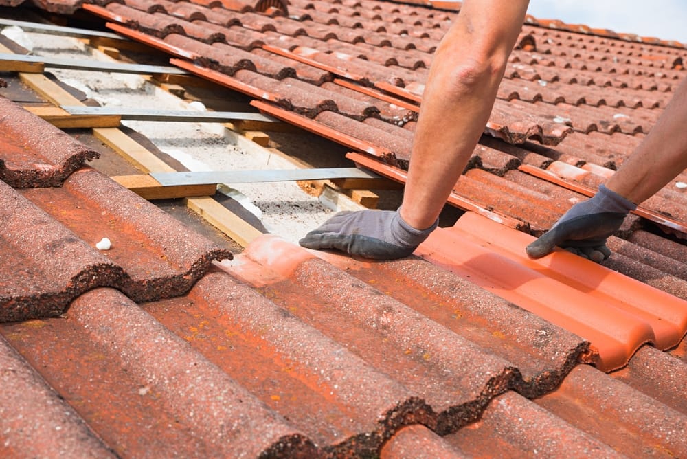 A roofing technician replaces damaged clay tiles on a residential roof, carefully aligning new tiles into place. The scene shows close-up hands-on repair work during a full roof replacement project. – Roof Replacement in Indianapolis