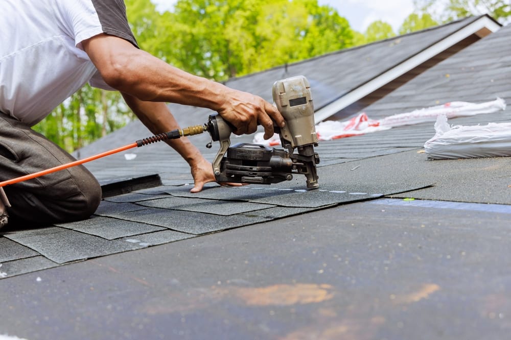 A contractor uses a pneumatic nail gun to fasten asphalt shingles during a commercial roof installation. The detailed shot emphasizes precision, durability, and high-quality craftsmanship – Commercial Roofing in Indianapolis.
